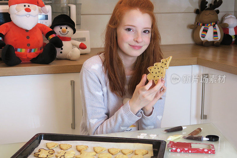 14 / 15岁的红发少女穿着白色衣服，现代厨房里展示着她用糖霜装饰的圣诞饼干